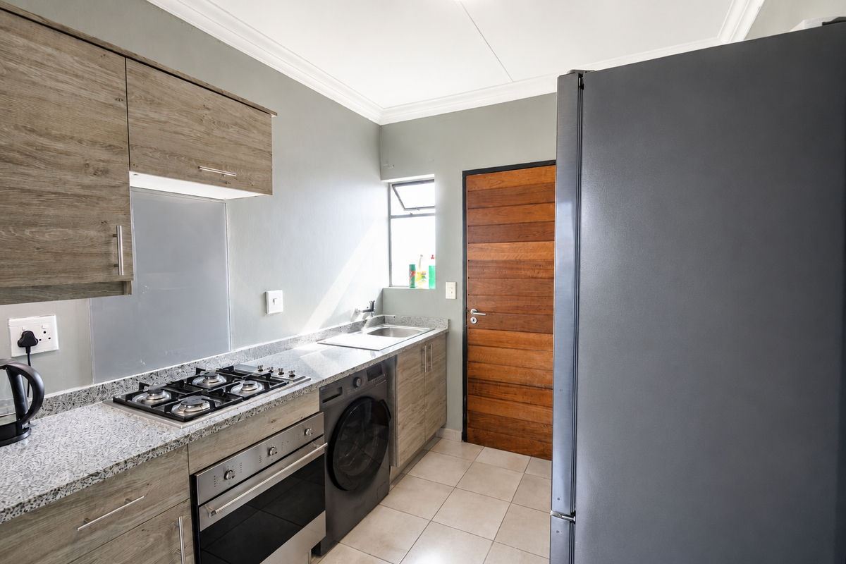 Modern kitchen featuring wood-finish cabinetry, granite countertops, integrated gas hob, built-in oven, and tiled flooring with direct access to an exterior door.