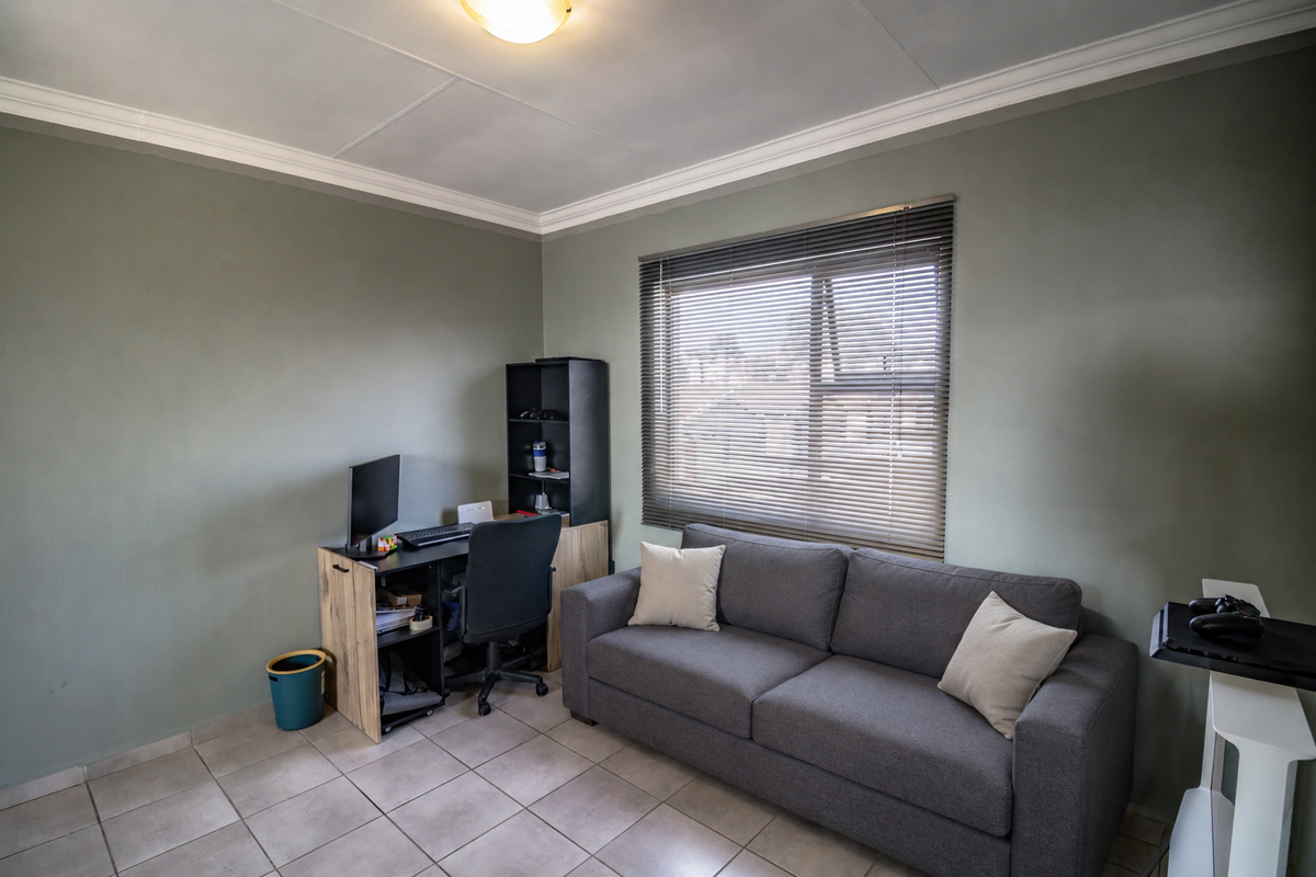 A functional office space featuring tiled flooring, neutral wall tones, and a window fitted with venetian blinds.