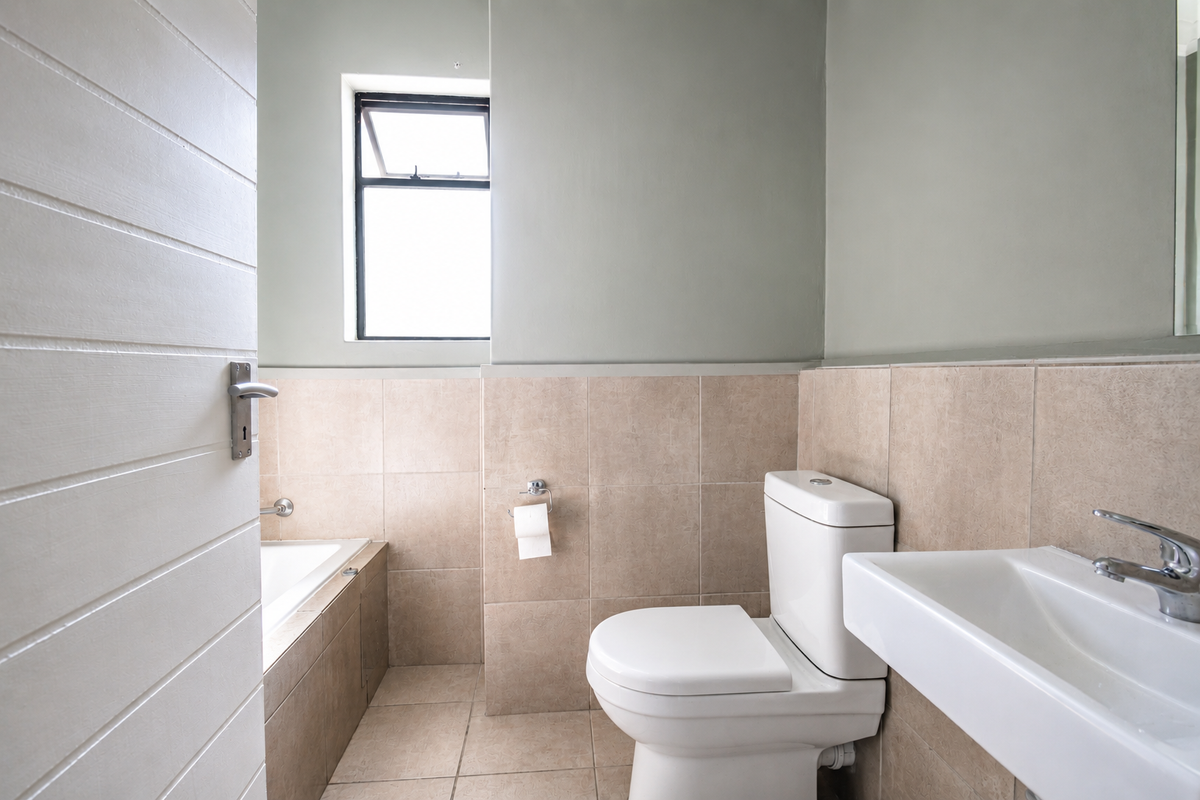 A clean, functional bathroom featuring neutral ceramic tiling, a built-in bathtub, a modern toilet, and a wall-mounted basin with chrome fixtures.