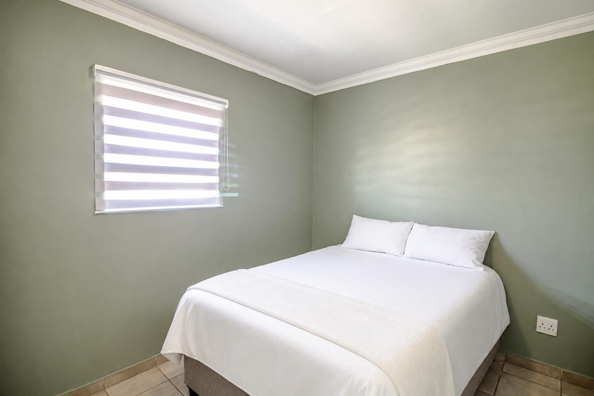 A clean and well-maintained bedroom featuring sage green walls, tiled flooring, crown molding, and modern zebra blinds.