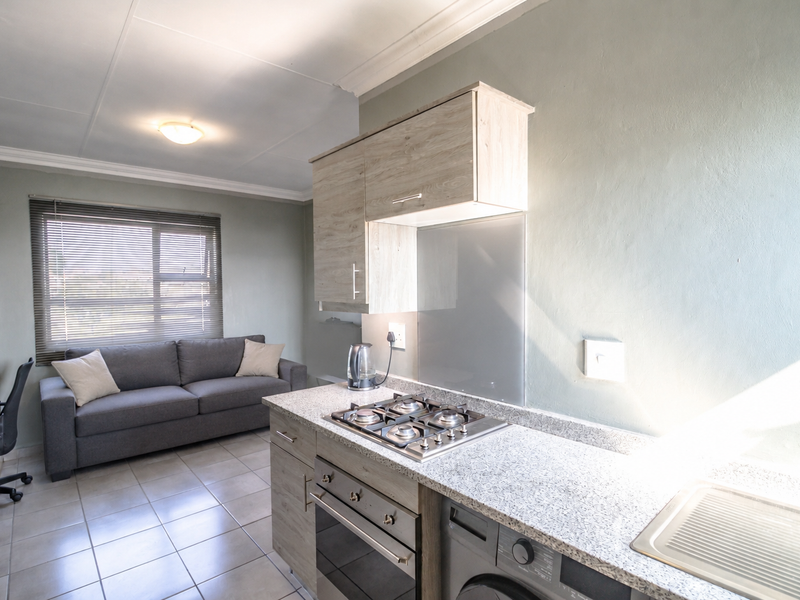 Open-plan living area featuring a modern kitchen with gas hob, built-in oven, granite countertops, and tiled flooring, seamlessly integrated with a comfortable lounge space.