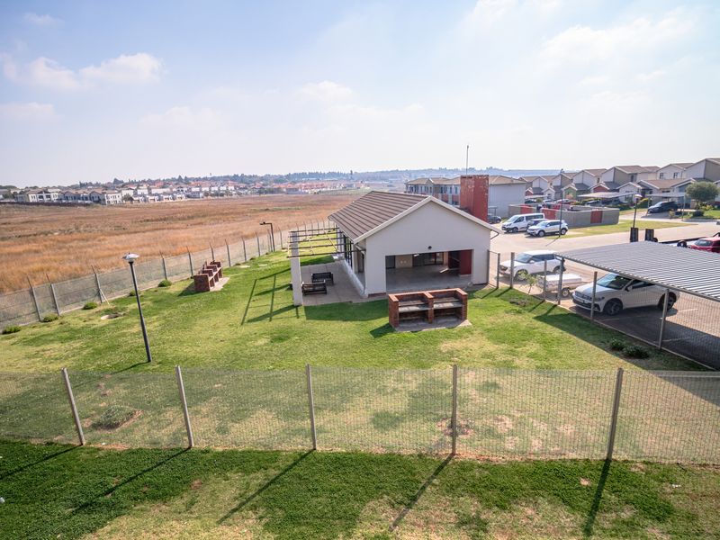Aerial view of a residential clubhouse facility featuring a covered patio, outdoor brick braai areas, and an adjacent carport within a secure complex.