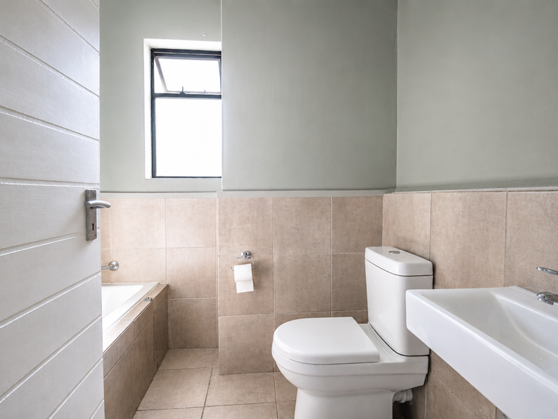 A clean, functional bathroom featuring neutral ceramic tiling, a built-in bathtub, a modern toilet, and a wall-mounted basin with chrome fixtures.