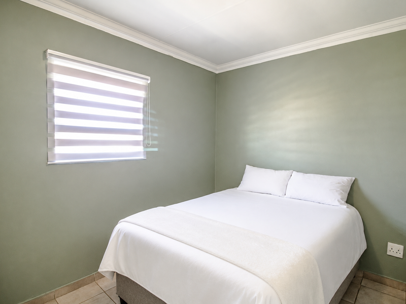A clean and well-maintained bedroom featuring sage green walls, tiled flooring, crown molding, and modern zebra blinds.