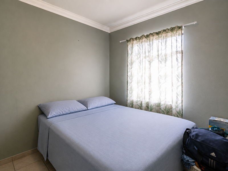 A compact bedroom featuring sage green walls, crown molding, and tiled flooring, providing a neutral foundation for interior design updates.