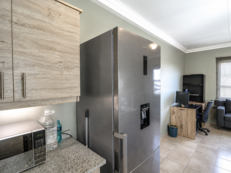 Open plan kitchen area featuring light wood-look cabinetry, granite countertops, and tiled flooring, seamlessly transitioning into a multi-purpose living and workspace.