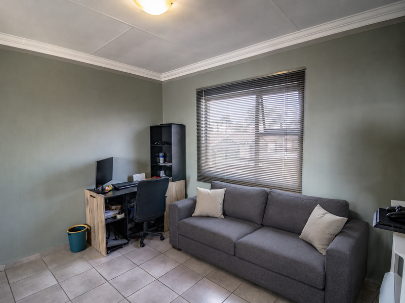 A functional office space featuring tiled flooring, neutral wall tones, and a window fitted with venetian blinds.