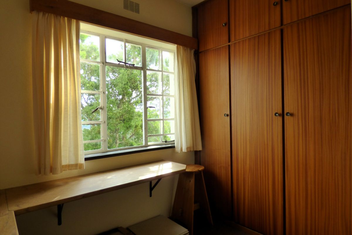 A bedroom featuring extensive built-in wooden cabinetry, a fixed desk area, and a window providing natural light and garden views.