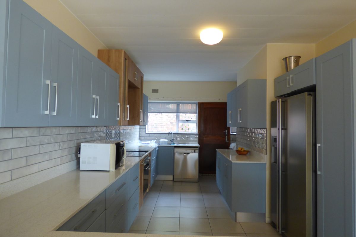 A modern galley-style kitchen featuring light blue cabinetry, stone countertops, subway tile backsplash, and stainless steel appliances.