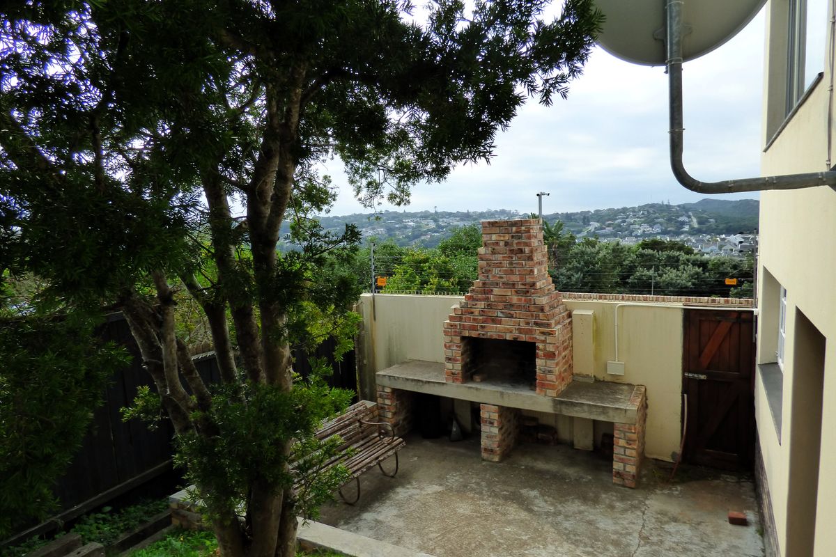 Rear outdoor area featuring a built-in brick braai, concrete patio, and perimeter wall with electric fencing, offering elevated views of the surrounding neighborhood.