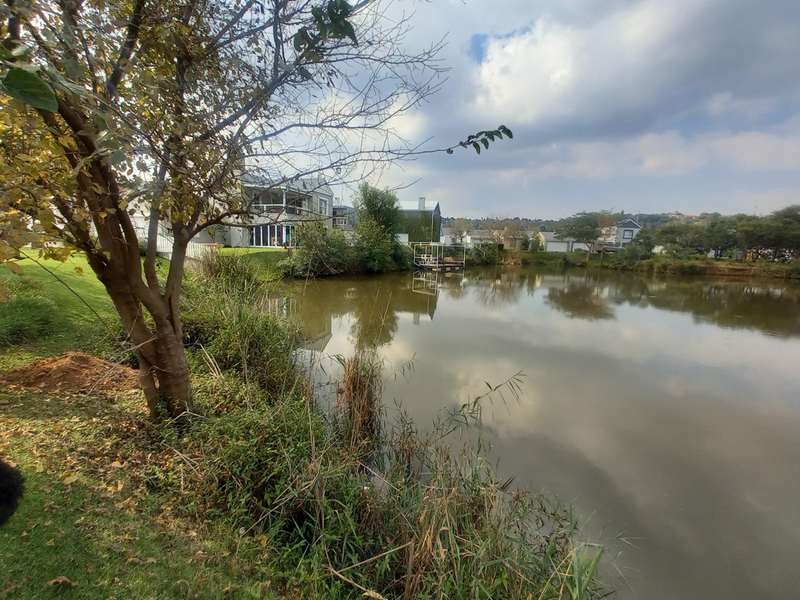 A scenic view of a tranquil lake surrounded by landscaped greenery and residential properties in the background.