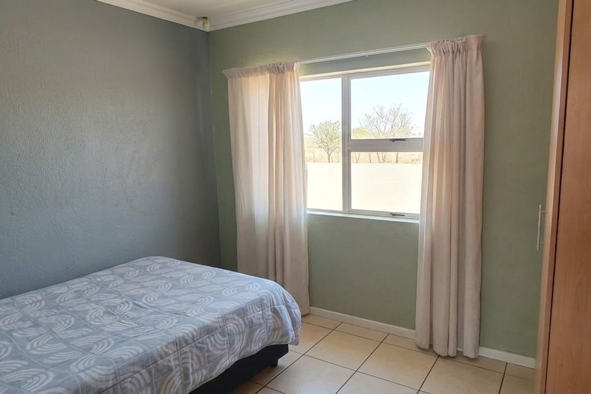 A standard bedroom featuring tiled flooring, built-in wooden cabinetry, and a window providing natural light.