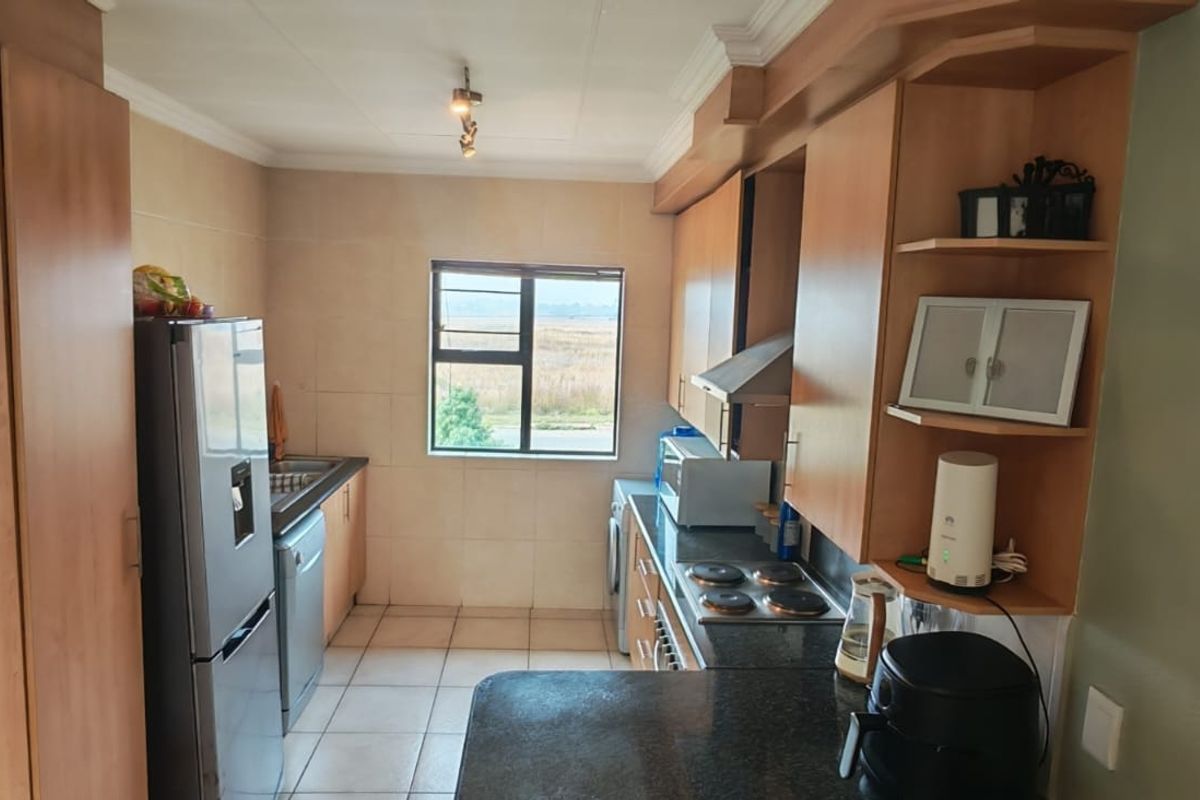A functional kitchen featuring wood-tone cabinetry, dark countertops, a built-in hob, and an extractor fan, with tiled flooring and a window providing natural light.