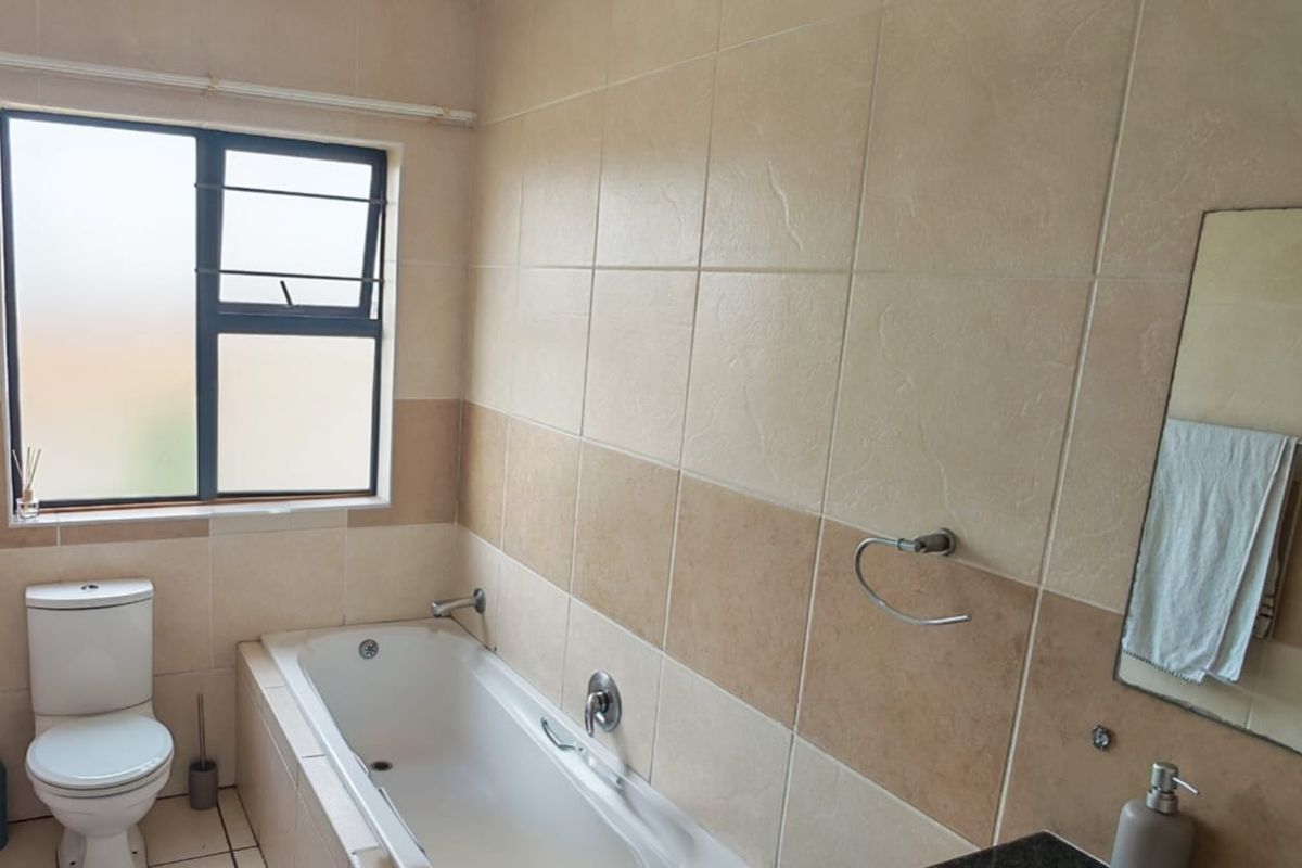 A functional bathroom featuring a built-in bathtub, a standard toilet, and wall-mounted fixtures with neutral tiled walls.