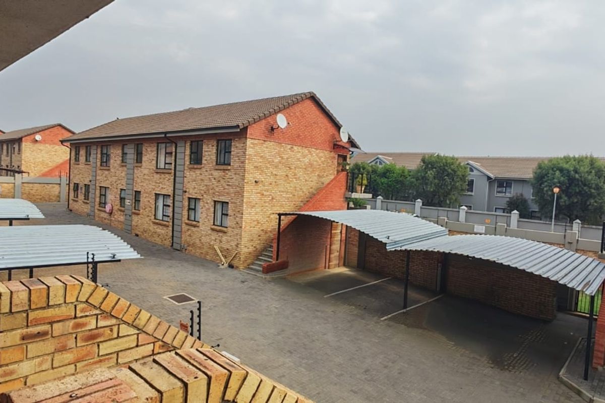 View of the apartment complex exterior, featuring face-brick buildings, paved parking area, and covered carports.