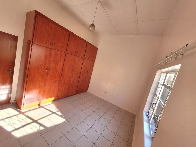 A vacant bedroom featuring tiled flooring, built-in wooden cupboards, and a window fitted with security bars.