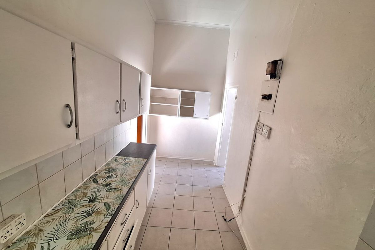 A functional, empty kitchen area featuring built-in cabinetry, tiled flooring, and a tiled backsplash, ready for modernization.