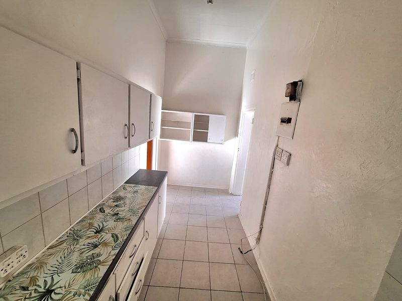 A functional, empty kitchen area featuring built-in cabinetry, tiled flooring, and a tiled backsplash, ready for modernization.