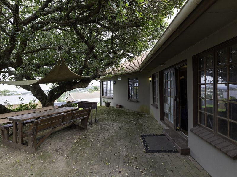 A paved outdoor patio area featuring timber-framed windows and sliding door access, shaded by a large mature tree.