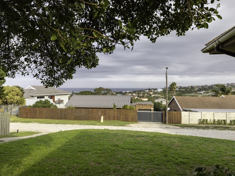 An elevated view overlooking the surrounding neighbourhood with distant sea views, featuring established trees and residential fencing.