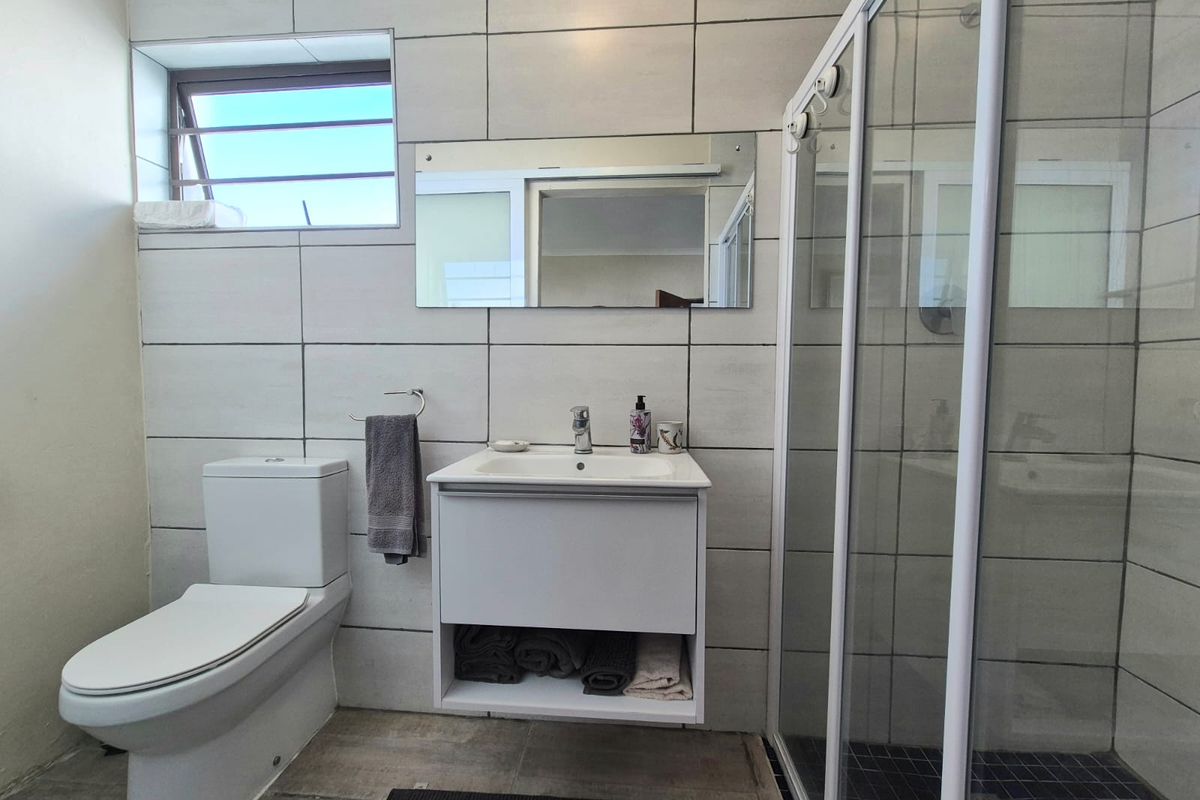 A modern bathroom featuring a wall-mounted vanity, a glass-enclosed shower, a toilet, and large-format wall tiles with a window for natural light.