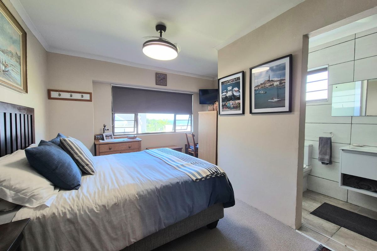 A well-maintained bedroom featuring neutral tones, a ceiling fan, and an adjoining en-suite bathroom with modern tiling and vanity.