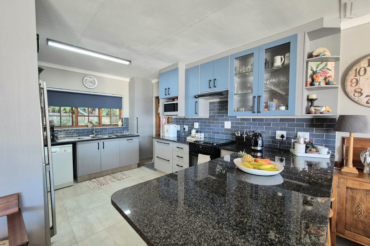 A well-appointed kitchen featuring granite countertops, blue and grey cabinetry, a subway tile backsplash, and a functional breakfast bar island.