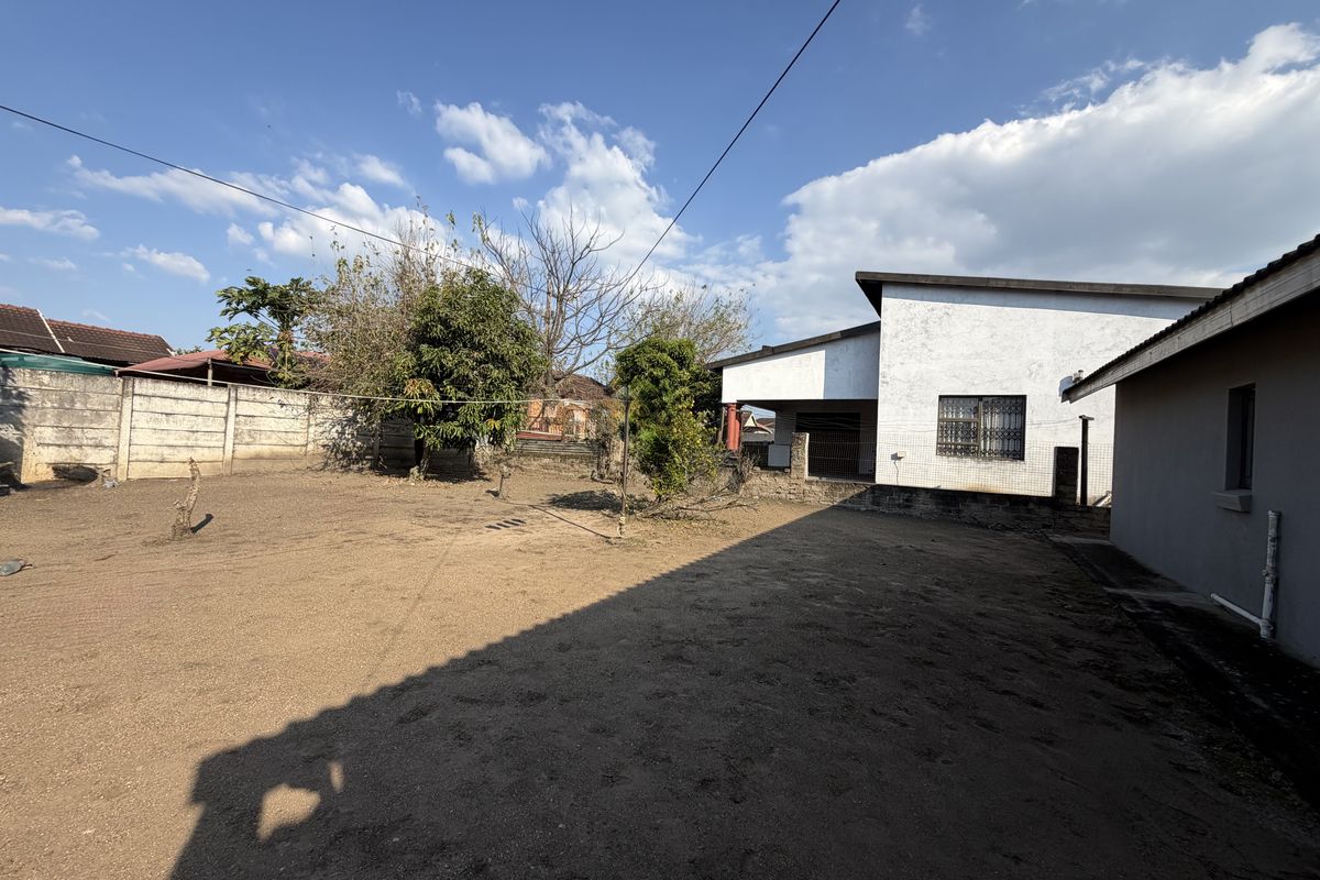 A spacious rear yard area featuring a large unpaved ground surface, perimeter boundary walls, and views of the rear building elevation.