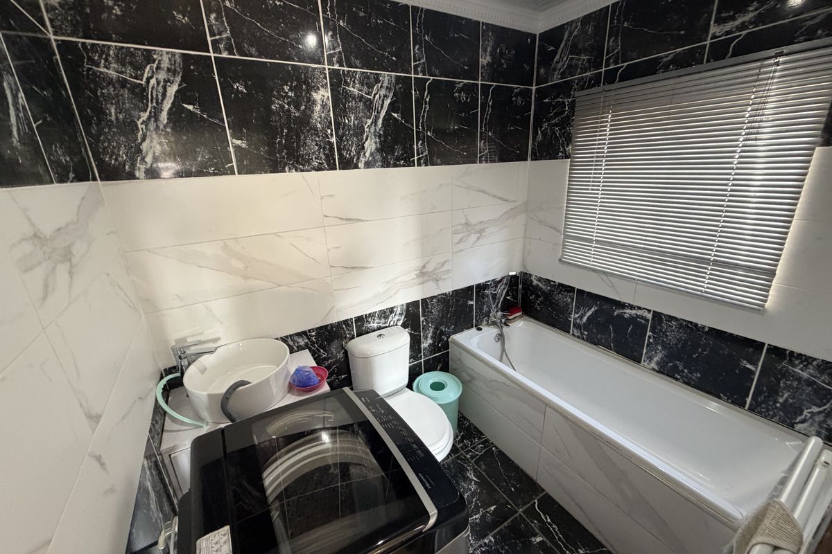 A compact bathroom featuring black and white marble-effect wall and floor tiling, a built-in bathtub, a modern basin, and a toilet.