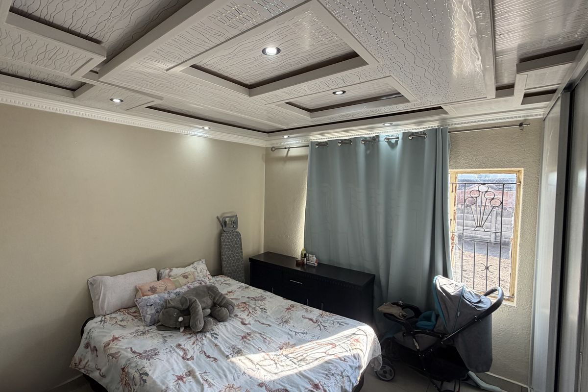 A bedroom featuring a decorative coffered ceiling with recessed lighting, tiled flooring, and a window with security bars.