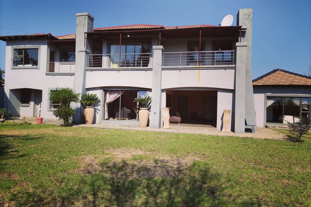 Rear view of a two-story house featuring a covered patio, upper-level balcony, tiled roof, and sliding glass doors opening to the garden.