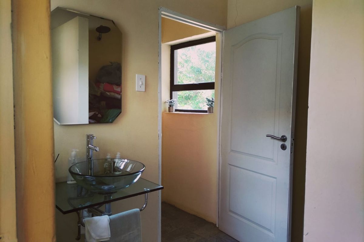 A functional bathroom featuring a glass vessel sink, chrome fixtures, and a wall-mounted mirror, with a doorway leading to an adjacent space.
