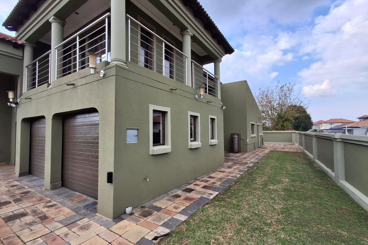 Rear view of the property featuring a double garage, an upper-level balcony with stainless steel railings, and a paved garden walkway.