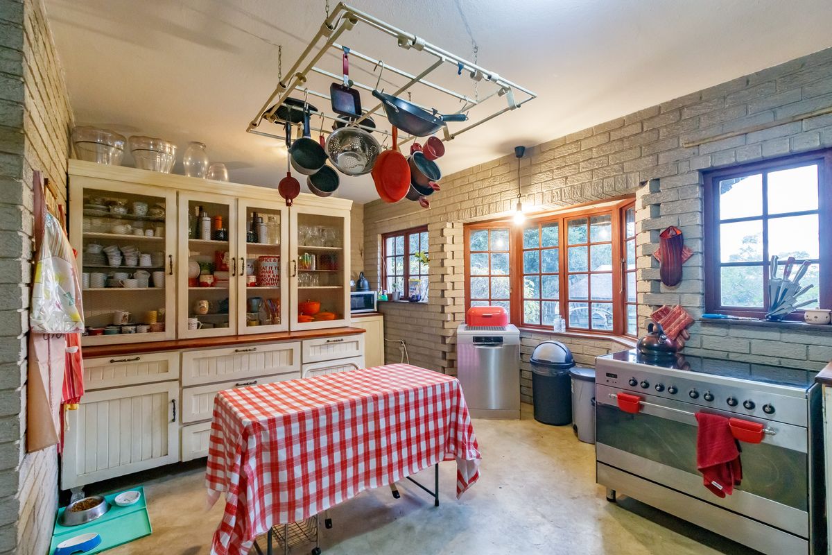 A rustic kitchen featuring exposed brick walls, timber-framed windows, built-in cabinetry, and a central hanging pot rack.