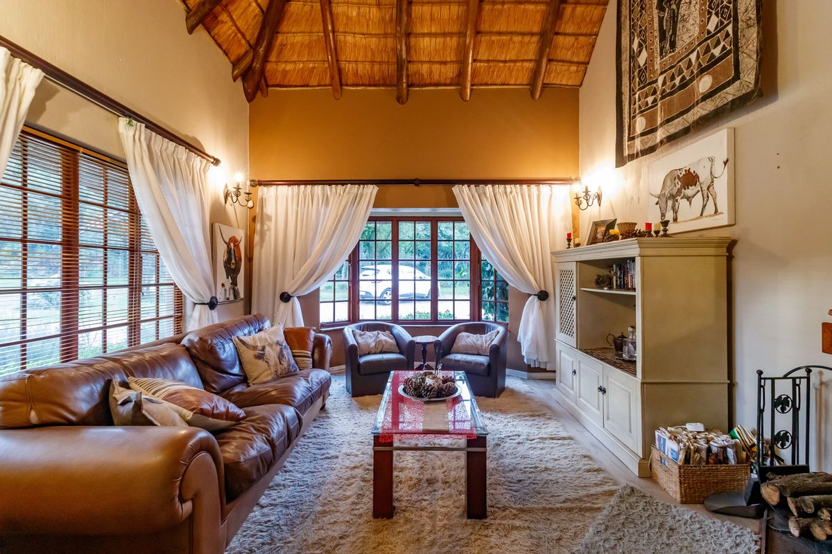 Cozy living room featuring a high vaulted thatched ceiling with exposed timber rafters, large windows, and warm ambient wall lighting.