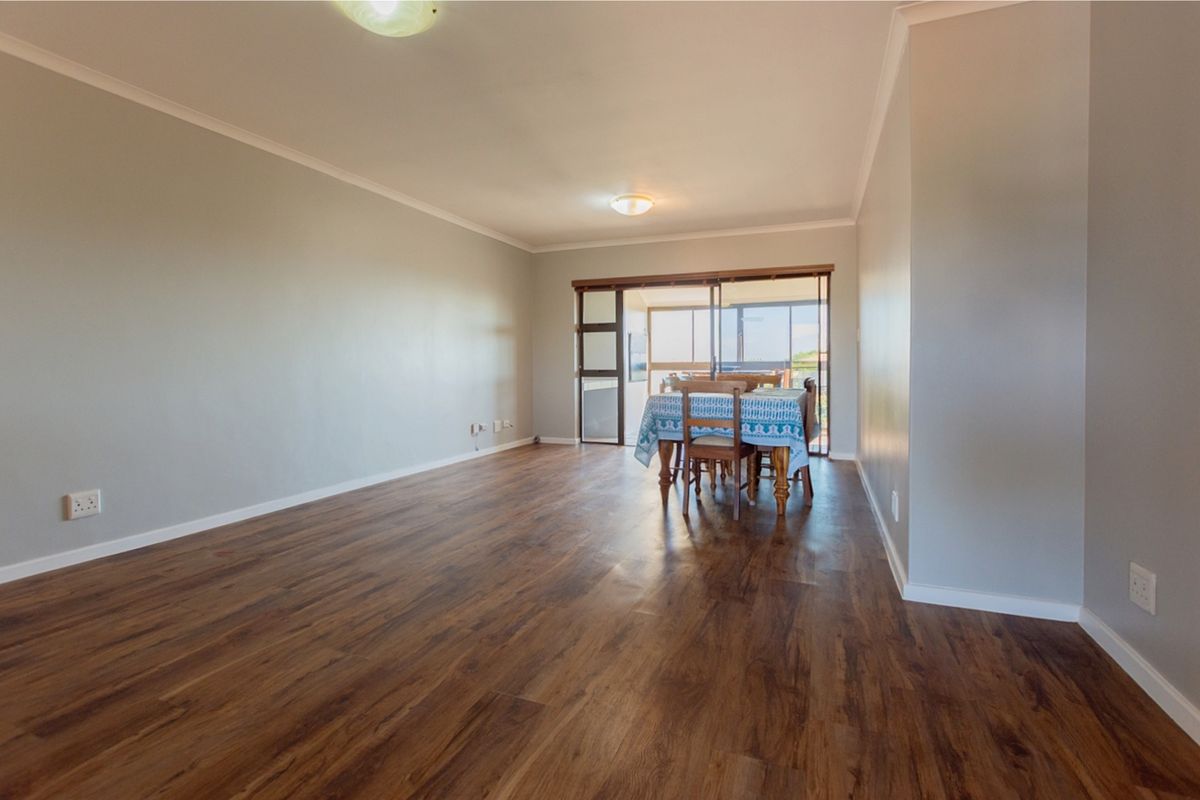 Spacious living area featuring modern laminate flooring, neutral walls, and a large sliding glass door providing access to the balcony.