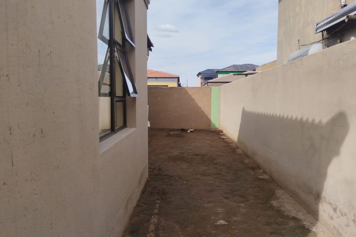 A narrow side or rear yard area featuring a high boundary wall and unlandscaped ground, offering potential for garden development or paving.
