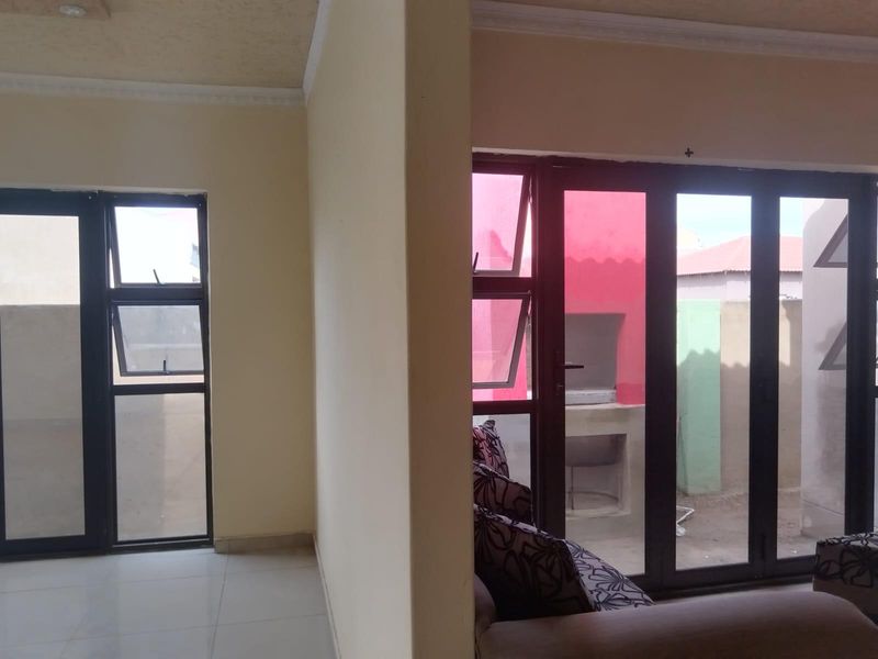 Living area featuring tiled floors and large aluminium framed doors providing direct access to an outdoor patio area with a built-in braai.