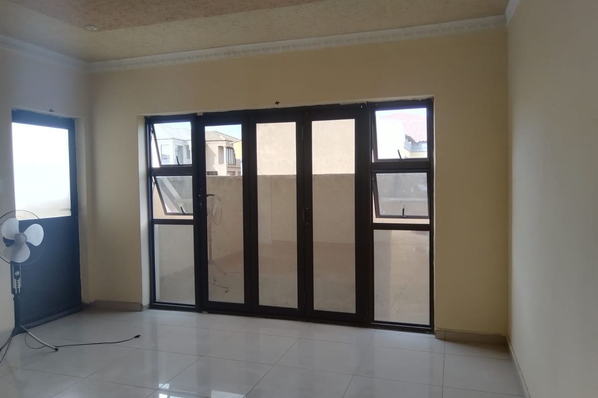 An empty living room featuring tiled flooring, recessed ceiling lights, and large aluminium-framed sliding doors providing access to an outdoor area.