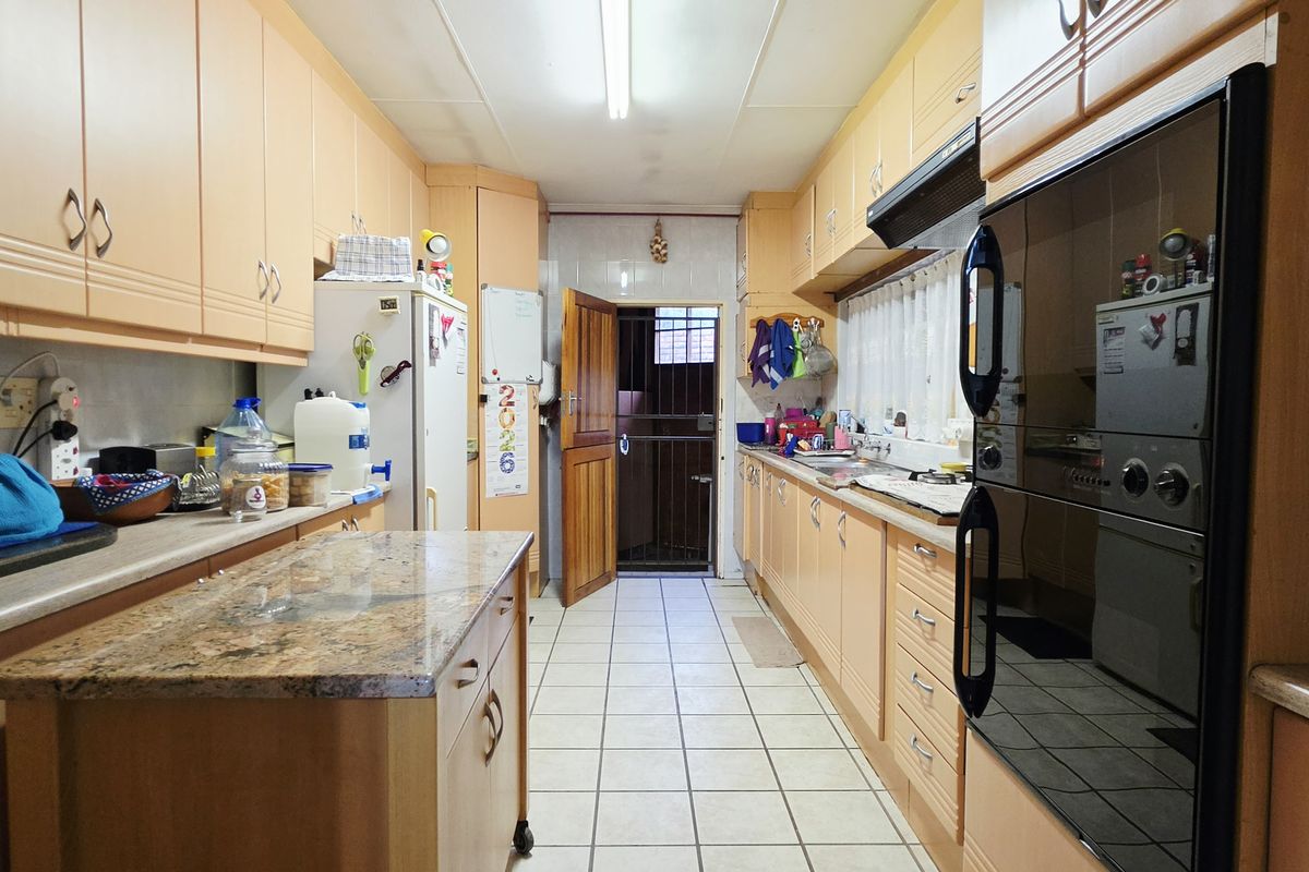 A functional galley-style kitchen featuring extensive wooden cabinetry, granite countertops, a built-in double oven, and tiled flooring with direct access to the rear exterior.