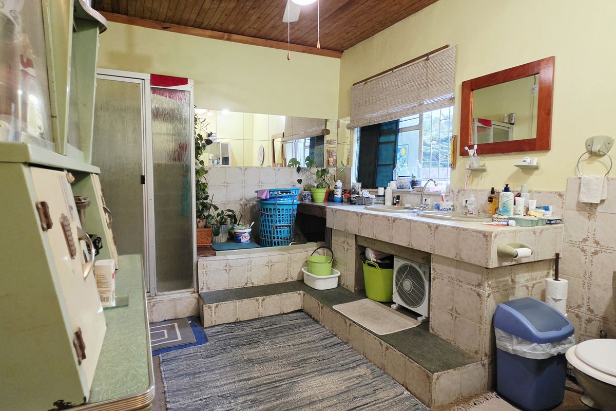 A dated bathroom featuring a raised tiled vanity area, shower enclosure, and toilet, with wood-paneled ceilings and original ceramic tiling.
