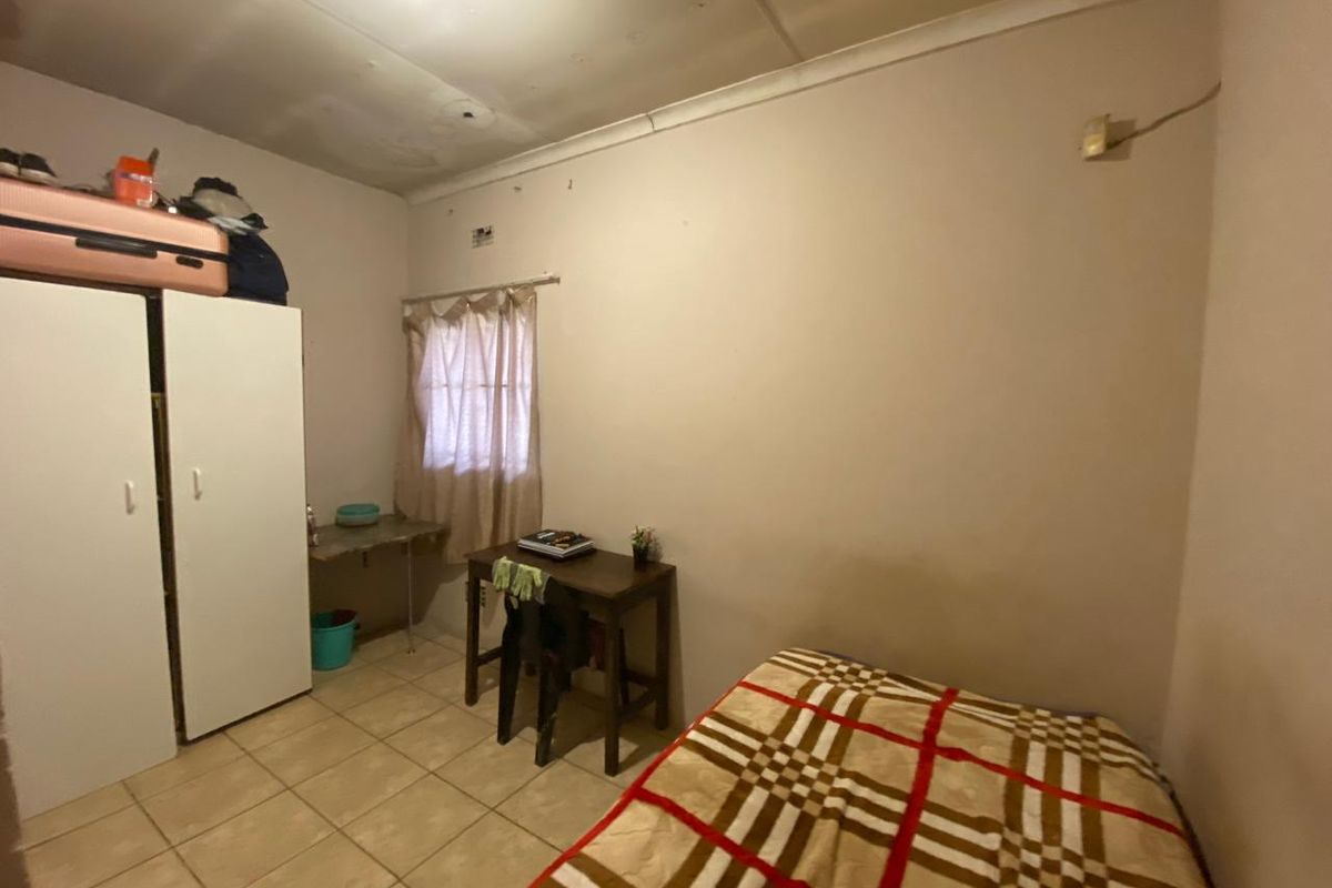 A functional bedroom featuring tiled flooring, a built-in wardrobe, and a window with natural light, offering a blank canvas for potential cosmetic updates.