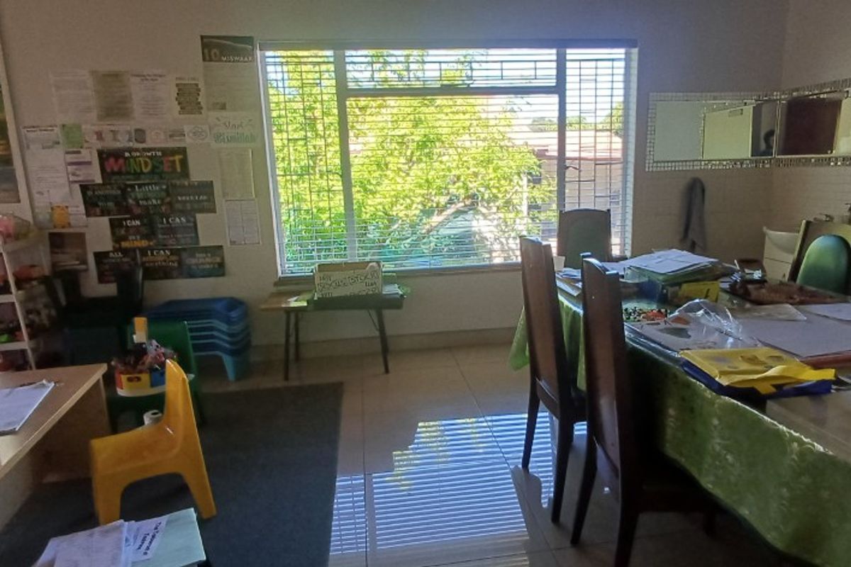 A functional living area featuring tiled flooring, large windows with security bars, and ample natural light, suitable for a variety of uses.