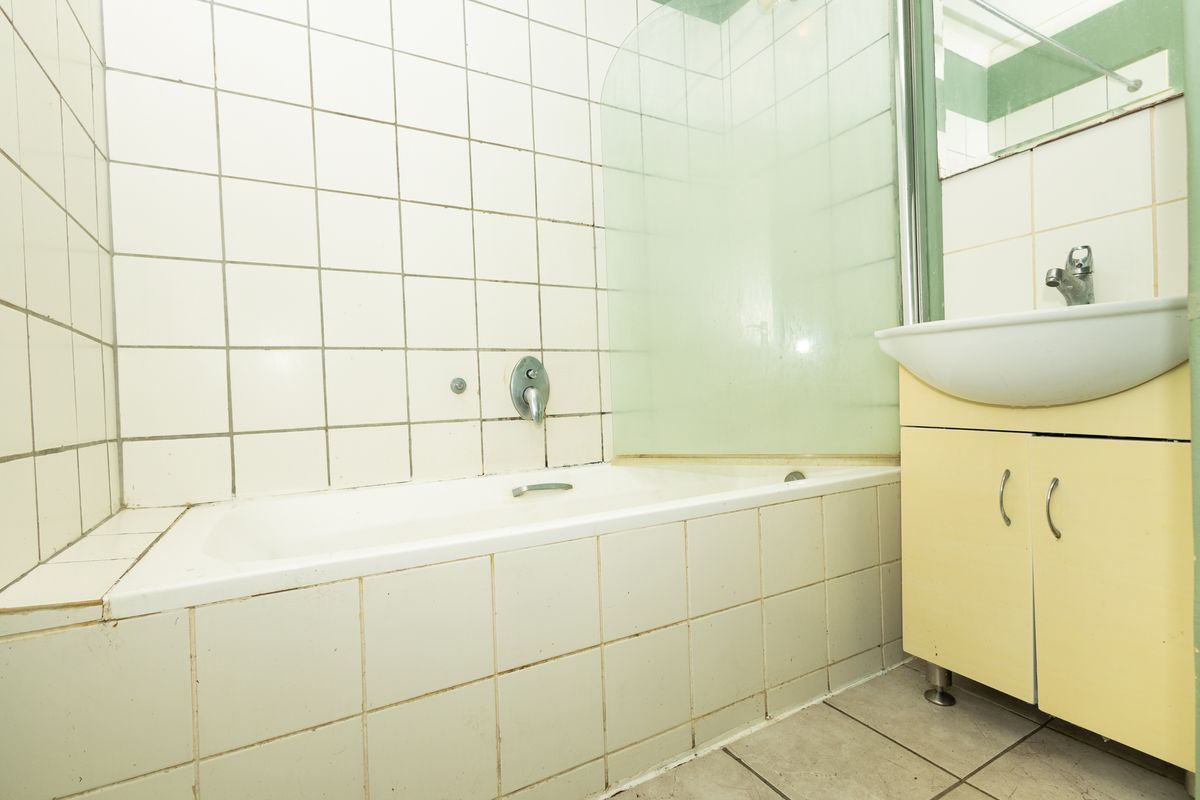 A dated bathroom featuring a built-in bathtub with a glass shower screen and a vanity unit with a basin.