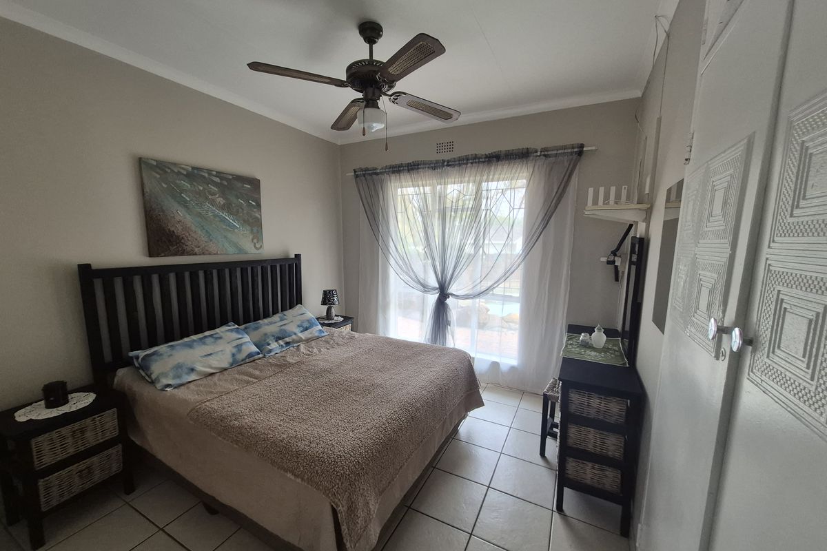 A functional bedroom featuring tiled flooring, a ceiling fan, and a sliding glass door providing natural light and access to the exterior.