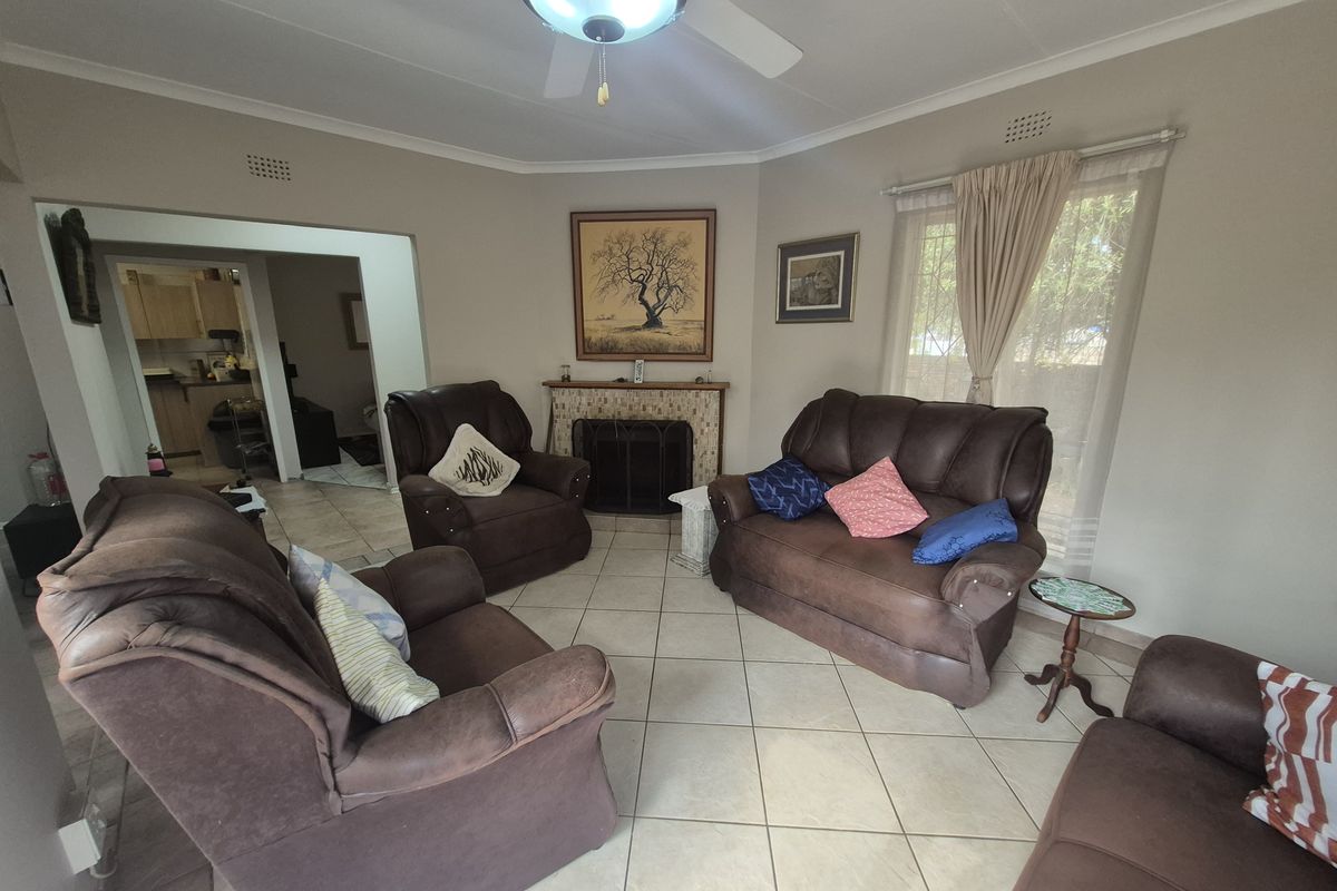A comfortable living room featuring tiled flooring, a central ceiling fan, and a fireplace, with an open transition leading into the kitchen area.
