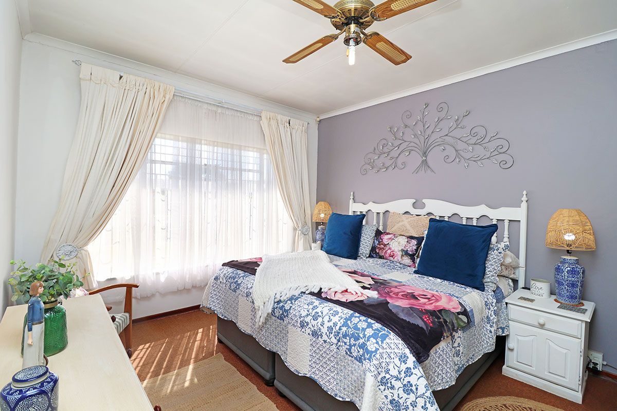 A well-lit bedroom featuring a ceiling fan, neutral wall tones, and large windows with curtain rails, providing a comfortable and functional sleeping space.