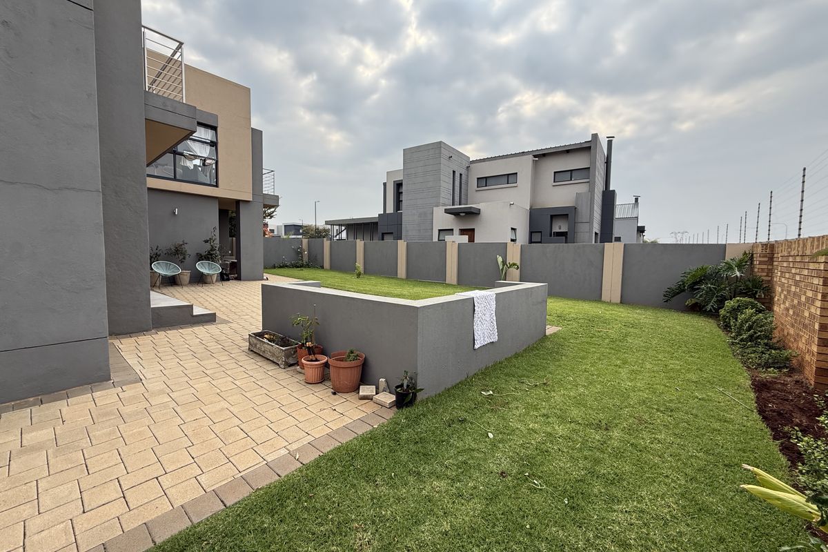 A well-maintained rear garden featuring a paved patio area, manicured lawn, and secure boundary walls with electric fencing.