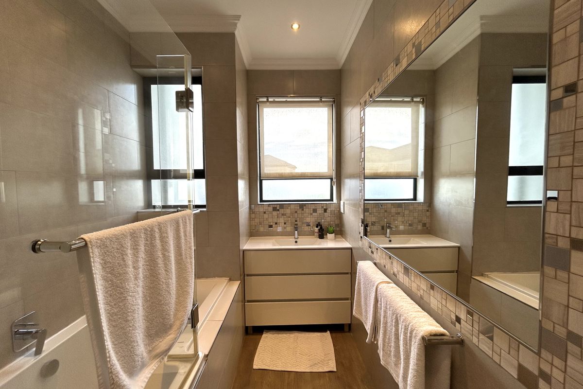 Modern bathroom featuring a built-in vanity with basin, large wall-mounted mirror, and a combined bathtub and shower area with tiled finishes.