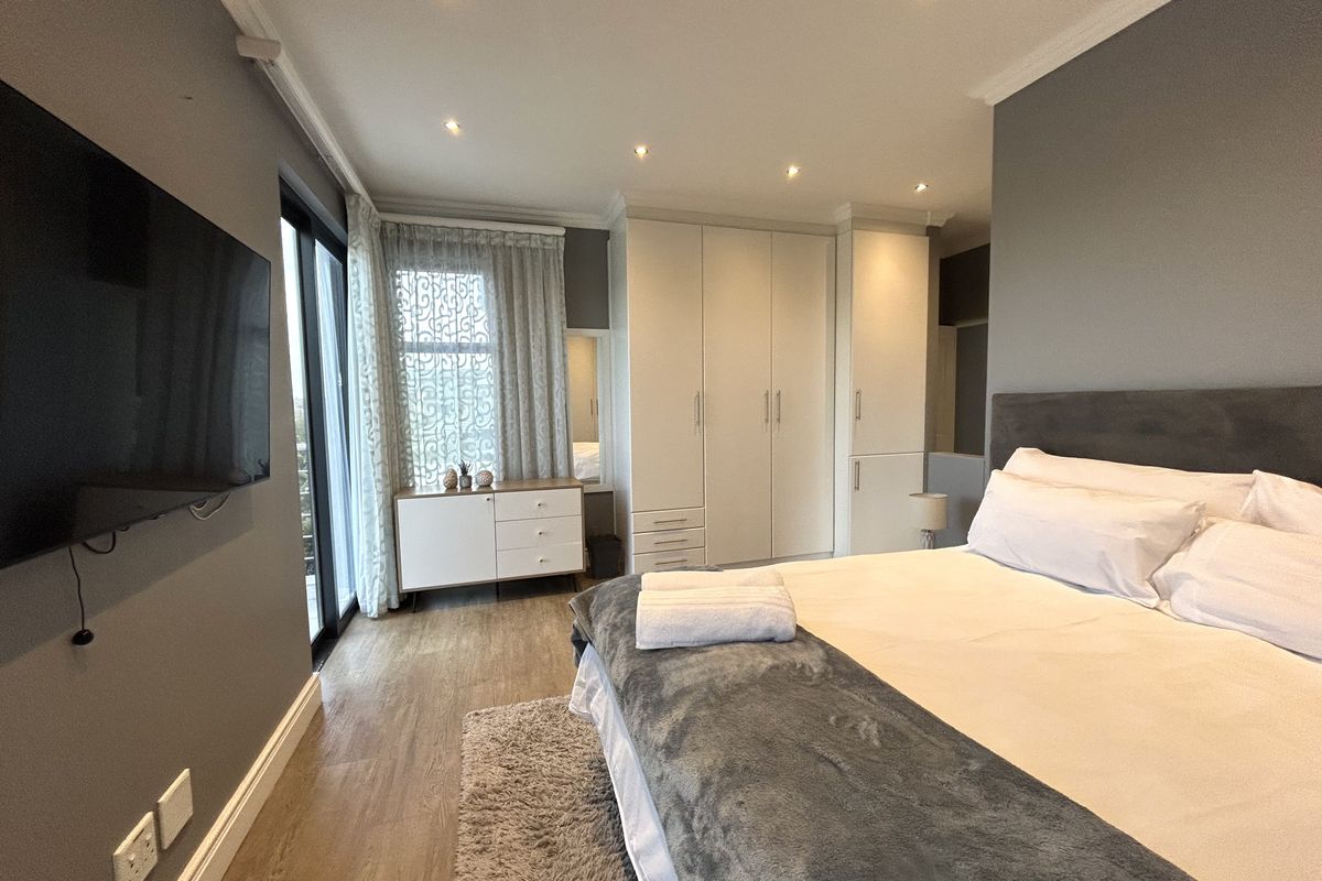 A well-maintained bedroom featuring built-in floor-to-ceiling wardrobes, recessed downlighting, and direct access to a private balcony through sliding glass doors.
